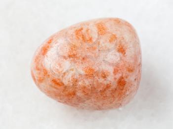 macro shooting of natural mineral rock specimen - tumbled sunstone (heliolite) gem stone on white marble background from USA