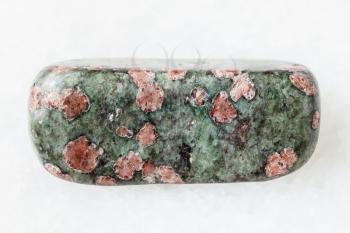 macro shooting of natural mineral rock specimen - tumbled Eclogite gemstone on white marble background from Salma region, Kola peninsula, Russia