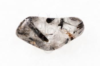 macro shooting of natural mineral rock specimen - tumbled quartz stone with Tourmaline crystals (tourmalinated quartz) on white marblebackground