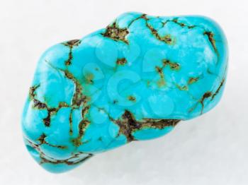 macro shooting of natural mineral rock specimen - tumbled blue howlite (turquenite) gem stone on white marble background