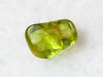 macro shooting of natural mineral rock specimen - tumbled Peridot gem stone on white marble background from Pakistan