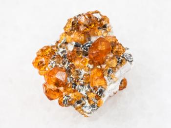 macro shooting of natural mineral rock specimen - raw crystals of spessartine garnet gemstone on white marble background from Fujian region, China
