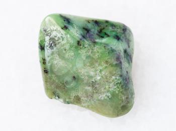 macro shooting of natural mineral rock specimen - tumbled green Grossular garnet gemstone on white marble background from South Africa