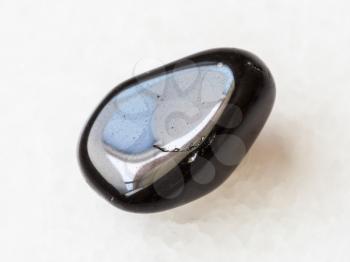 macro shooting of natural mineral rock specimen - tumbled black obsidian gem stone on white marble background from Mexico
