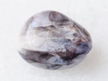 macro shooting of natural mineral rock specimen - tumbled Stone of Tamerlane (amethyst quartz) gemstone on white marble background from Tajikistan