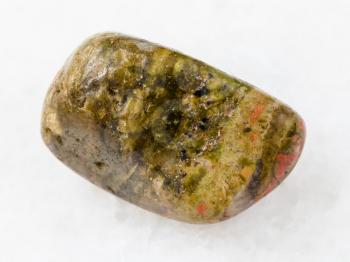 macro shooting of natural mineral rock specimen - tumbled unakite gem stone on white marble background from South Africa