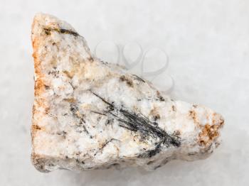 macro shooting of natural mineral rock specimen - black Ludwigite crystals in raw stone on white marble background from Praskovie-Evgenyevskaya mine, South Ural, Russia