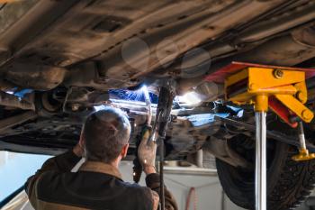 repairing of corrugation muffler of exhaust system in car workshop - serviceman welds the silencer on car by argon welding