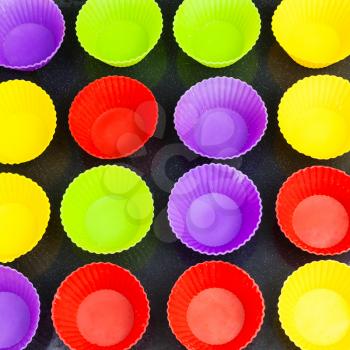 top view of many empty multicolor silicone molds for cupcakes on baking tray