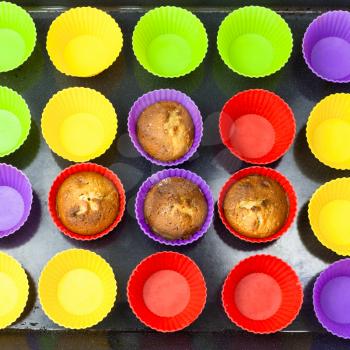 top view of few baked cupcakes and many empty multicolor silicone molds on dark tray