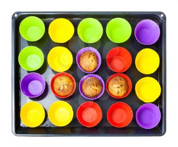top view of tray with few baked cupcakes and many empty multicolor silicone molds isolated on white background