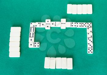 top view of gameplay of dominoes board game with white tiles on green baize table
