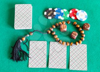 top view of card decks, dices, casino tokens and worry beads on green baize table
