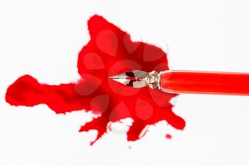 top view of steel nib in red dip pen over red ink blot on white paper