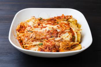 korean cuisine - kimchi appetizer (spice nappa cabbage) in white bowl on dark brown wooden board