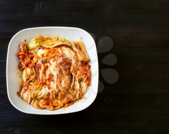 korean cuisine - above view of kimchi appetizer (spice nappa cabbage) in white bowl on dark brown wooden board with copyspace