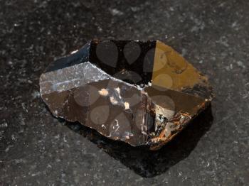 macro shooting of natural rock specimen - crystal of Cassiterite (Tin ore) stone on black granite background from Pravourmiyskoe deposit in Khabarovsk Krai, Russia