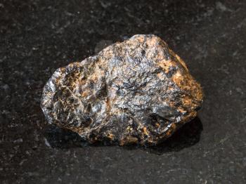 macro shooting of natural rock specimen - raw Cassiterite (Tin ore) stone on black granite background from Pravourmiyskoe deposit in Khabarovsk Krai, Russia