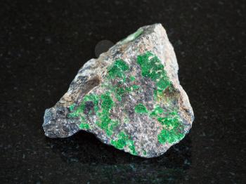 macro shooting of natural mineral - green Uvarovite crystals on rough Chromite stone on black granite from Ural Mountains