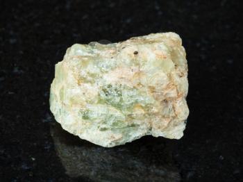 macro shooting of natural mineral - raw chrysoberyl (green beryl) crystal on black granite from Ural Mountains