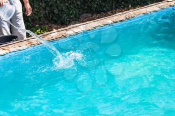 man pours of disinfectant in outdoor swimming pool on backyard of country house