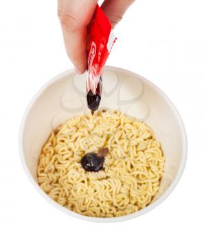 cooking instant noodles - squeezing curry sauce from packet into cup with instant noodles isolated on white background