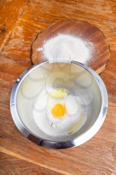 cooking of pie - pile of flour with broken egg in steel bowl and flour on wooden board