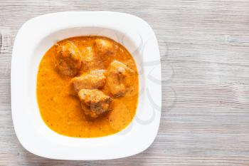 Indian cuisine - Murg Makhan Masala barbequed chicken pieces in spicy tomato and creamy curry sauce in white bowl on wooden table
