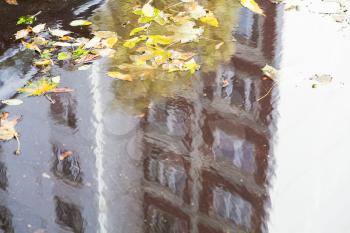 puddle on urban road with reflection of apartment house in sunny autumn day