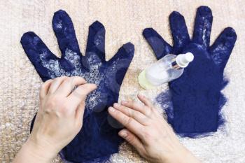 workshop of hand making a fleece gloves from blue Merino sheep wool using wet felting process - craftsman puts fibers on finger of glove on the cutting pattern