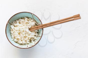 top view of chopsticks in bowl with boiled rice on white concrete board
