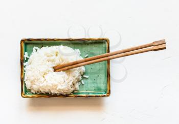 top view of boiled rice with chopsticks on green plate on white concrete board