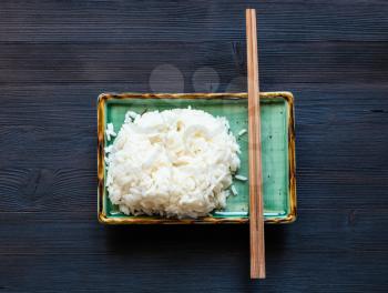 top view of portion of boiled rice and chopsticks on green plate on dark wooden board