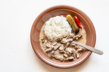 Russian cuisine dish - eating of Beef Stroganoff (Beef Stroganov, Befstroganov) pieces of stewed meat in sour cream with boiled rice on brown plate on white board