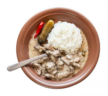 Russian cuisine dish - fork in Beef Stroganoff (Beef Stroganov, Befstroganov) pieces of stewed meat in sour cream with boiled rice on brown plate isolated on white background