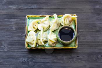 Chinese cuisine dish - top view of served portion of Dumplings with three fillings (shrimp, egg and greens) on green plate on dark wooden board