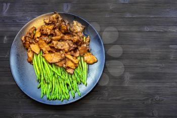 Chinese cuisine dish - top view of Beef fried in soy sauce with green asparagus on black plate on dark wooden board with copyspace