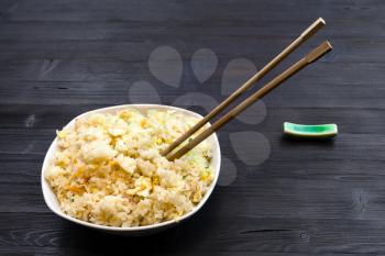 Chinese cuisine dish - portion of Fried Rice with Shrimps, Vegetables and Eggs (Yangzhou rice) with chopsticks on dark wooden table