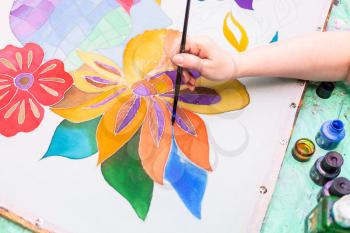 artist paints floral pattern on white silk canvas on wooden frame in cold contour batik technique
