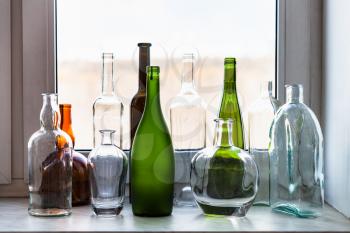 various empty bottles on windowsill and view of city park through home window on sunny spring day on background