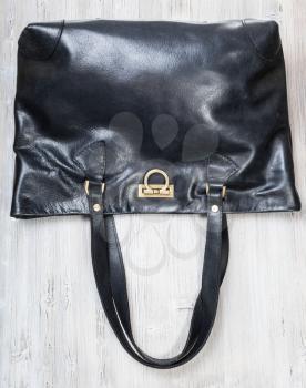 handcrafted black leather shopper bag with brass clasp on gray wooden table