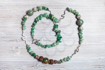 top view of handcrafted necklace from tumbled green aventurine gemstones, cracked agate, aplite, rhodonite and rudraksha beads on gray wooden table