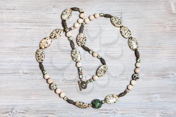 handcrafted necklace from aplite cabochons, glass beads, green serpentinite ball, cracked cacholong beads and brass inserts on gray wooden table