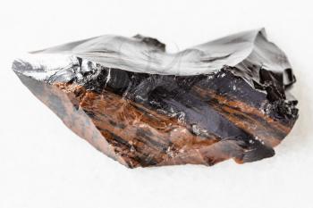macro photography of sample of natural mineral from geological collection - unpolished mahogany Obsidian (volcanic glass) from Armenia on white marble background