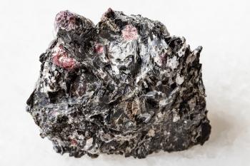 macro photography of sample of natural mineral from geological collection - unpolished red Garnet crystals in Biotite rock from Yelovyy Navolok, Shueretskoye deposit, Karelia, Russia on white marble