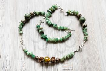 handcrafted necklace from tumbled green aventurine gemstones, cracked agate, aplite, rhodonite and rudraksha beads on gray wooden table