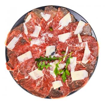 top view of portion of Carpaccio (thinly sliced raw beef fillet) decorated by Parmesan, Arugula and capers on black plate isolated on white background