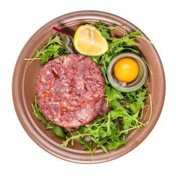 top view of Steak tartare (raw minced beef meat) and yolk in bowl on fresh greens on brown plate isolated on white background