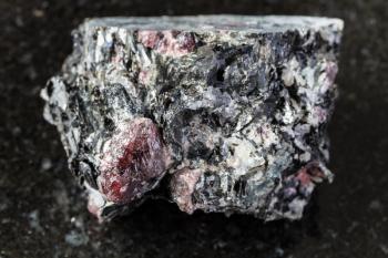 macro photography of sample of natural mineral from geological collection - raw Garnet crystals in Biotite rock from Yelovyy Navolok, Shueretskoye deposit, Karelia, Russia on black granite background