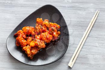 Korean Chinese cuisine - top view of Kkanpunggi spicy fried Chicken pieces with vegetables in sweet and sour sauce on black plate with chopsticks on gray board close up